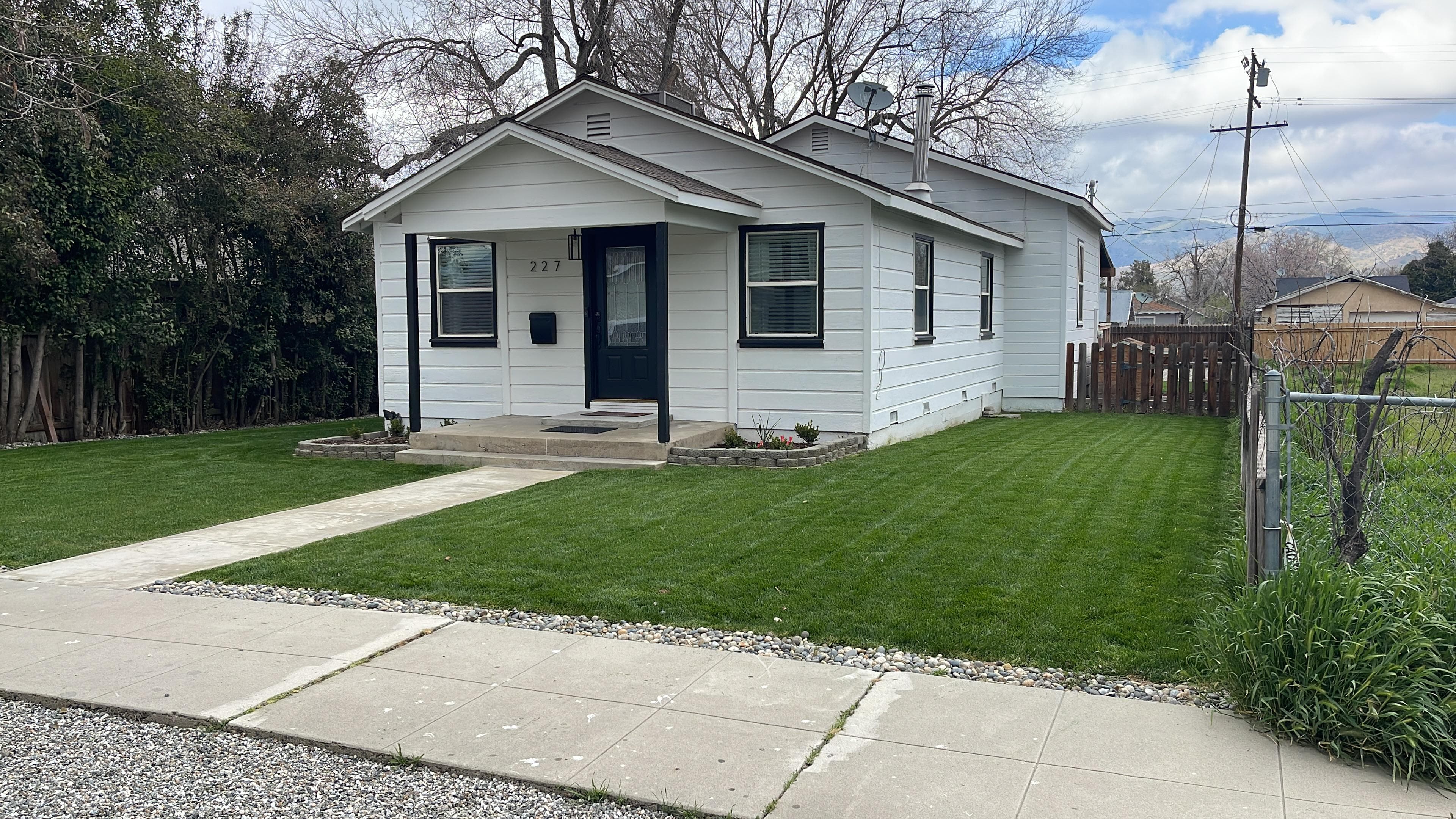 Small white house with black trim, a manicured green lawn, and a concrete walkway.