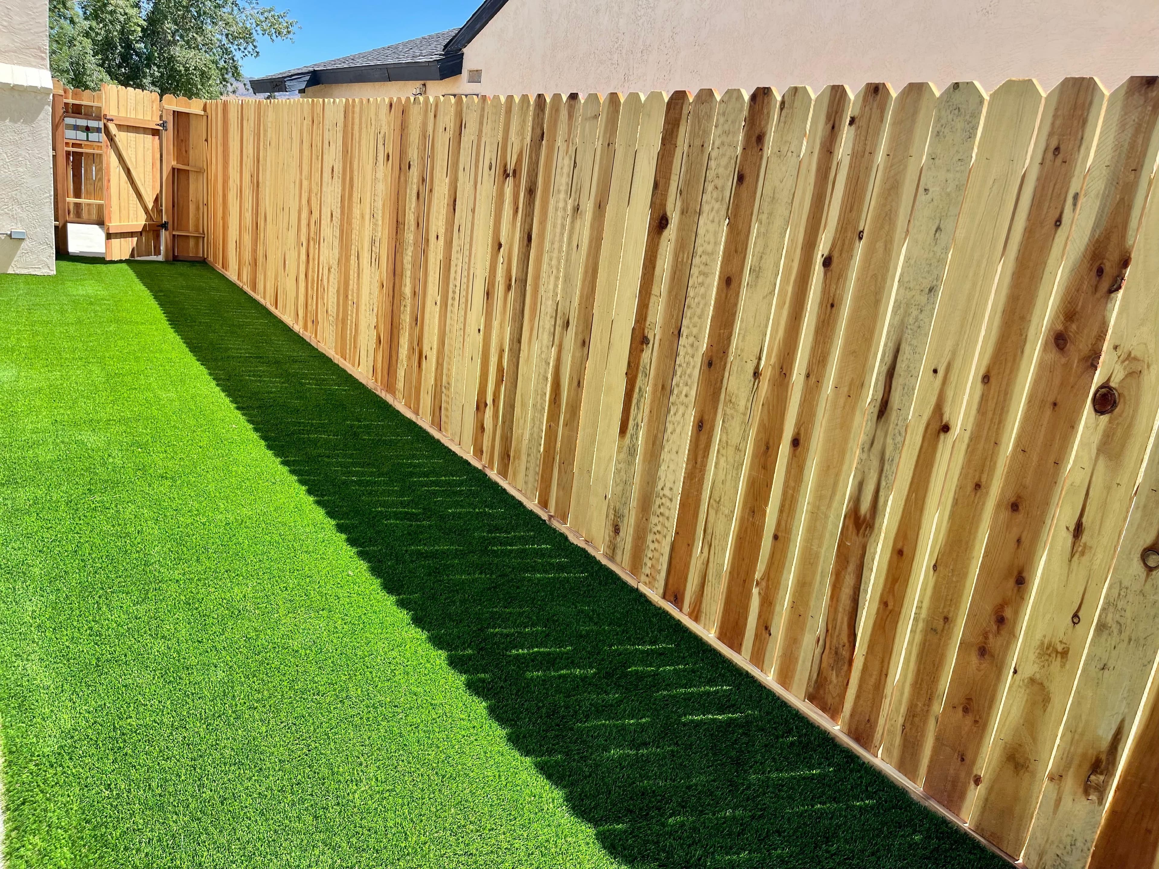 Long wooden dog-ear fence casting a shadow on a vibrant green artificial turf lawn.