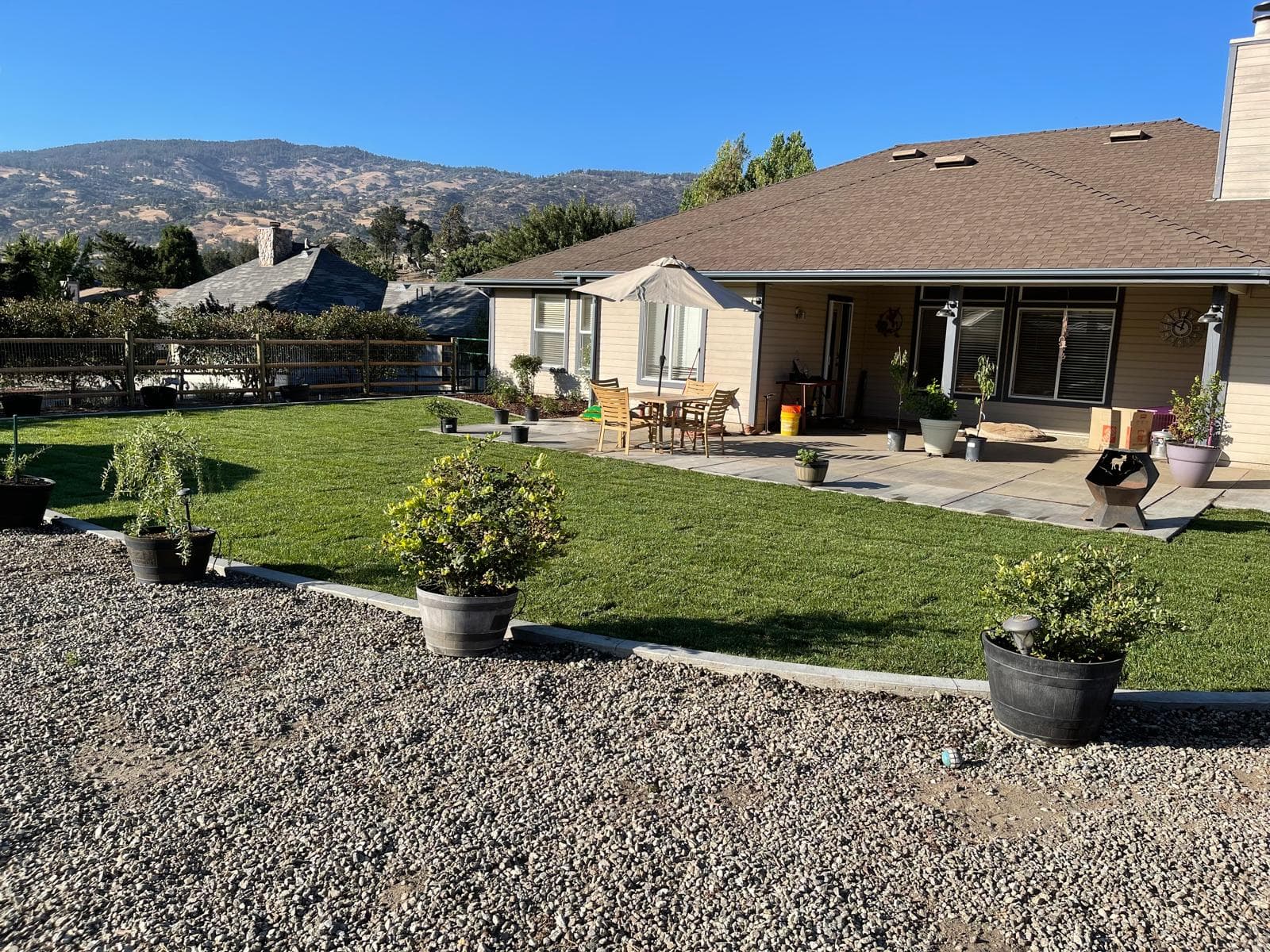 Sunny backyard featuring a green lawn, patio furniture, and distant mountain views.