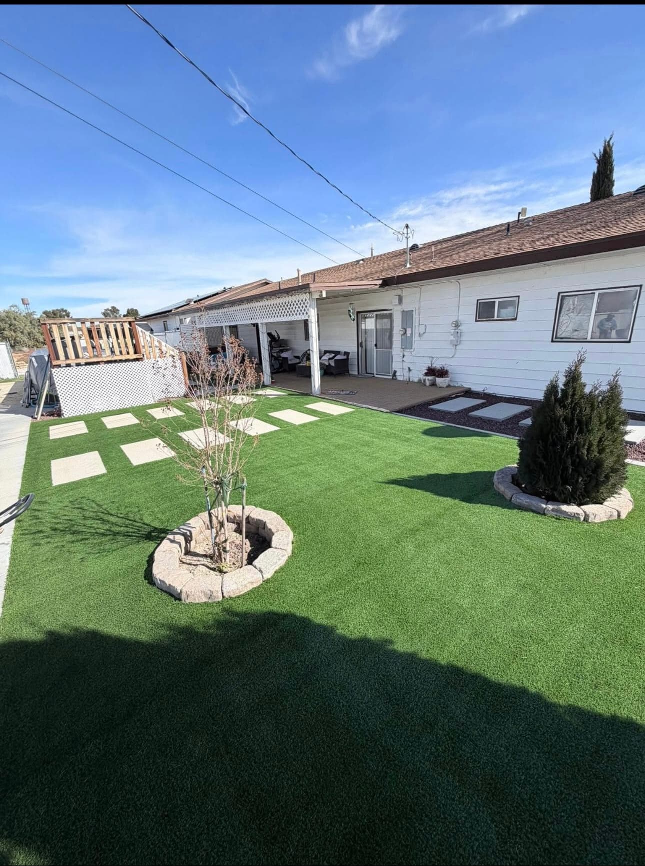 Backyard with artificial turf, square stepping stones, and small trees by a white house.