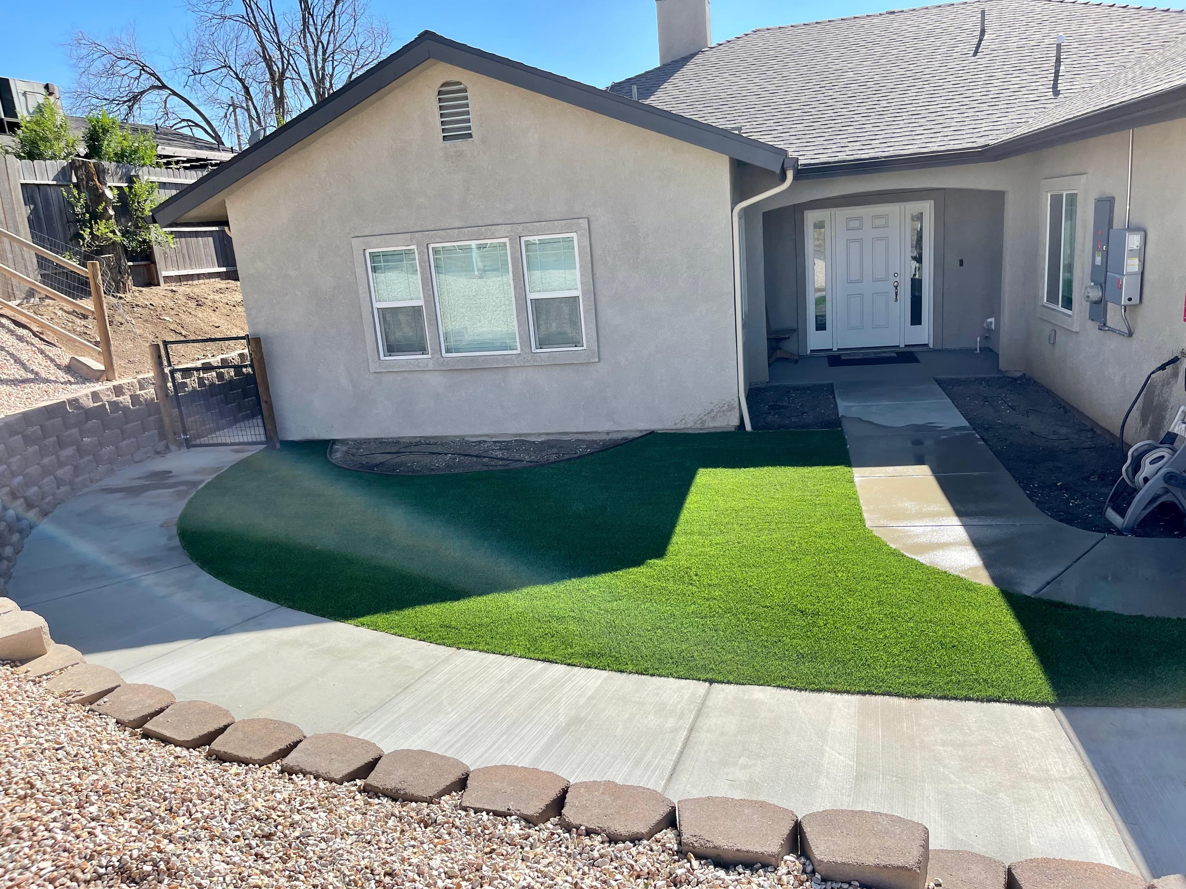 Beige stucco house with a white front door and a vibrant green artificial turf lawn.