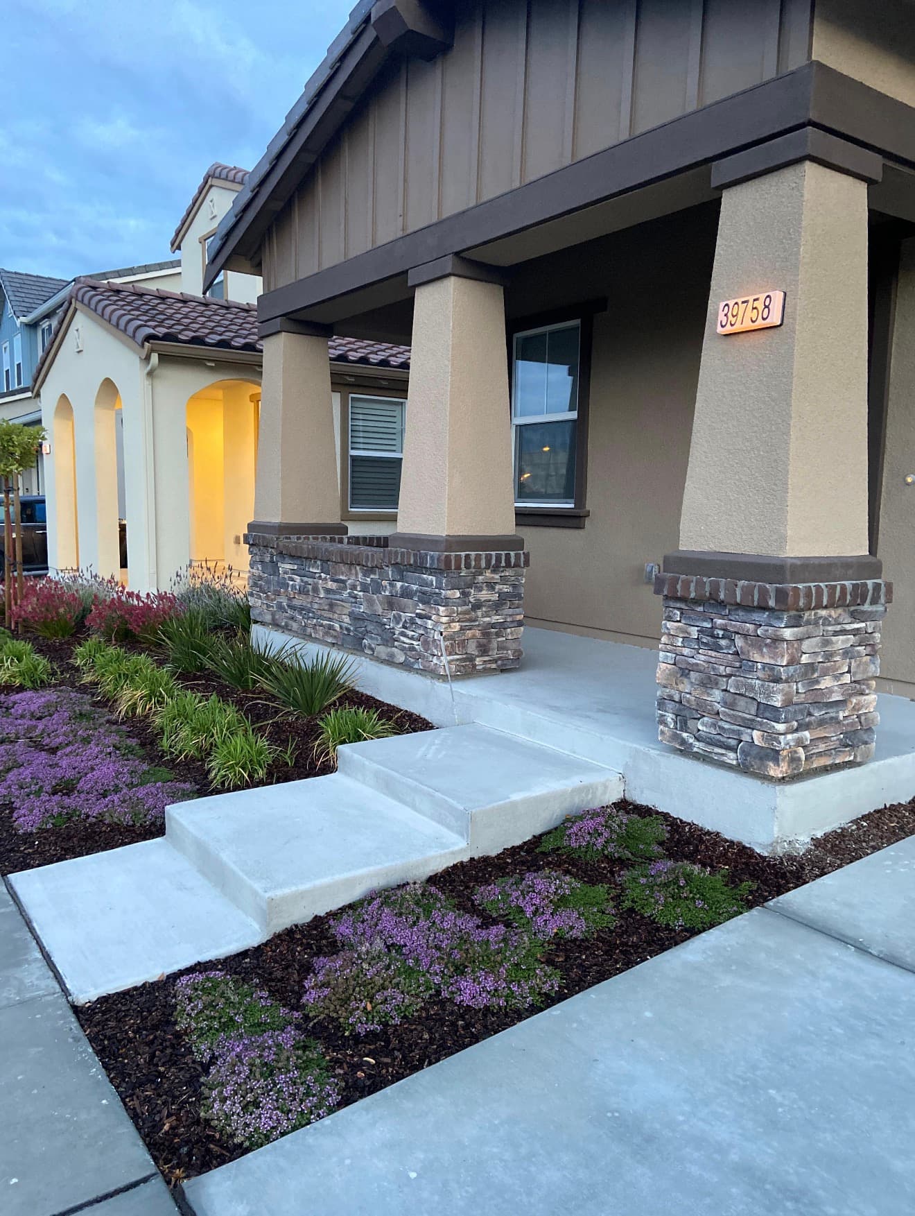 Modern house porch with stone pillars, concrete steps, and landscaped garden with purple flowers.